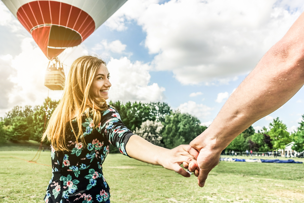 Happy young woman wants to take balloon tour holding boyfriend's hand
