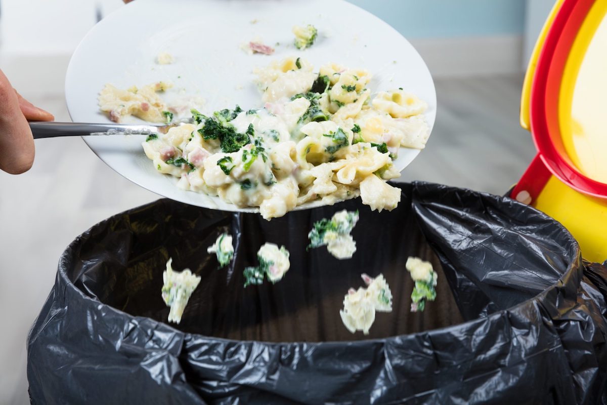 Close-up Of A Person Throwing The Leftover Pasta Into The Trash Bin And Creating Food Waste