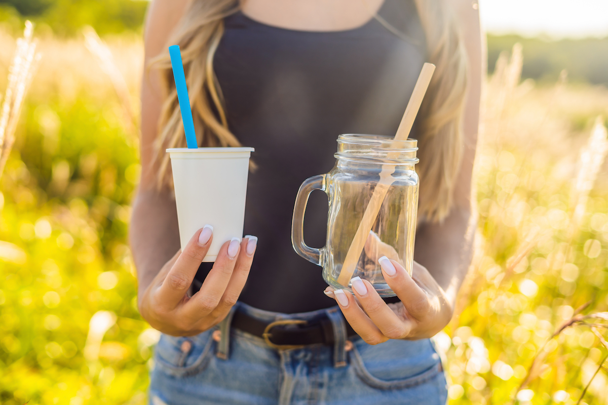 woman holding single use cup and straw in one hand and reusable cup and straw in the other hand