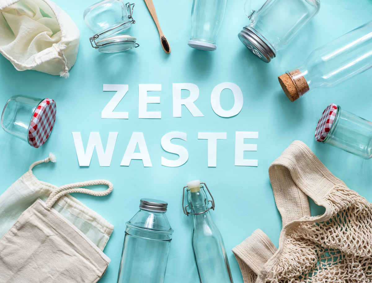 Zero waste concept. Textile eco bags, glass jars and bamboo toothbrush on blue background with Zero Waste white paper text in center. Eco friendly and reuse concept