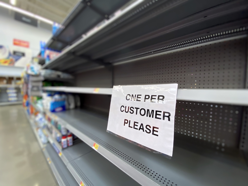 photo of empty grocery store shelves with sign saying one per customer please