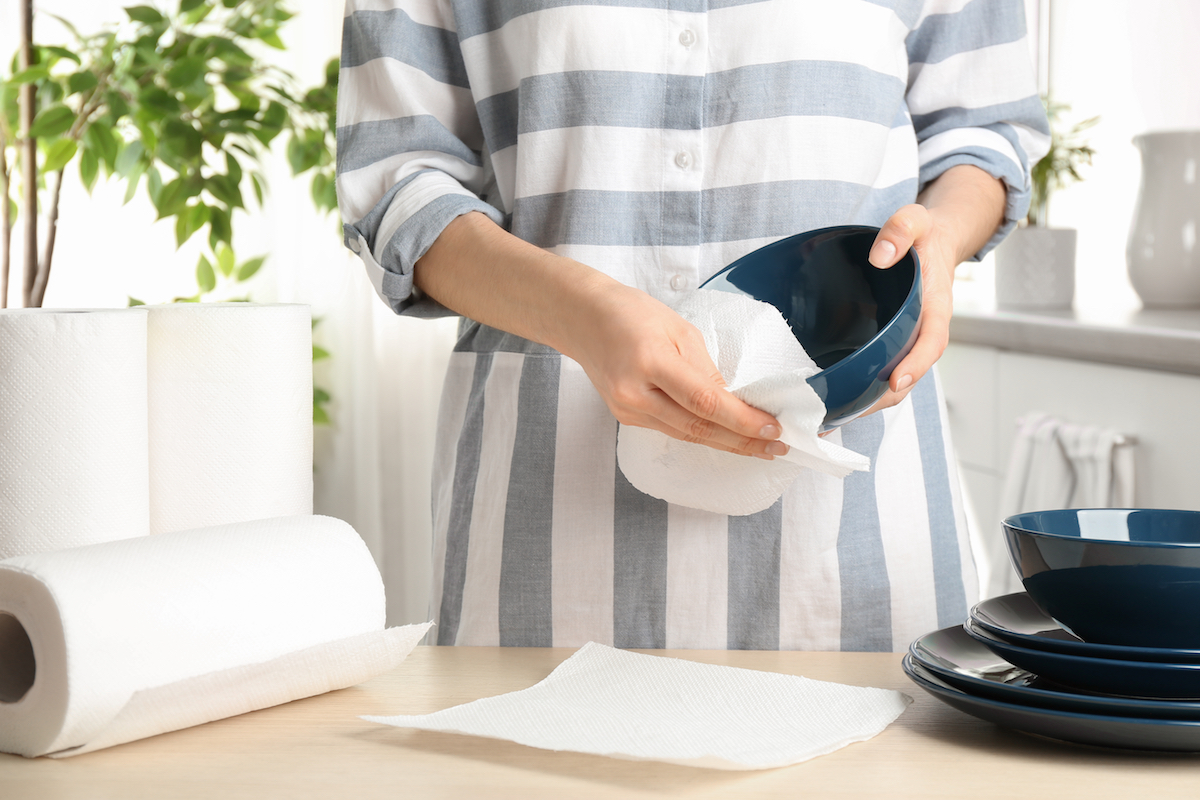 Woman wiping ceramic bowl with paper towel indoors, closeup